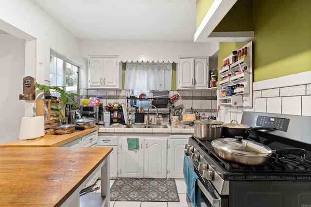 kitchen featuring stainless steel stove, tasteful backsplash, wooden counters, and white cabinetry