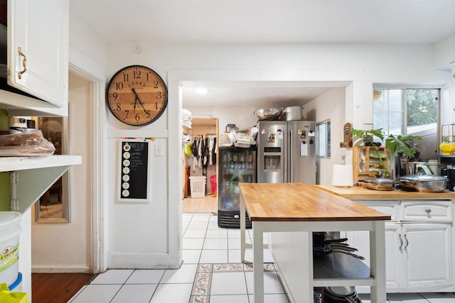 kitchen featuring butcher block countertops, light tile patterned floors, white cabinetry, and stainless steel fridge