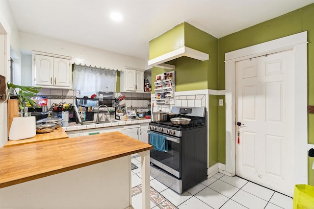 kitchen with light tile patterned flooring, tasteful backsplash, white cabinets, stainless steel gas stove, and butcher block countertops