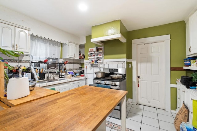 kitchen featuring tasteful backsplash, white cabinets, light tile patterned floors, stainless steel gas stove, and sink