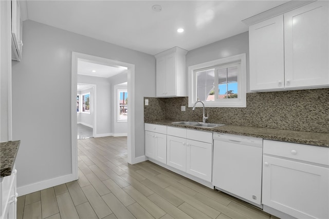 kitchen with white dishwasher, dark stone counters, white cabinetry, and sink