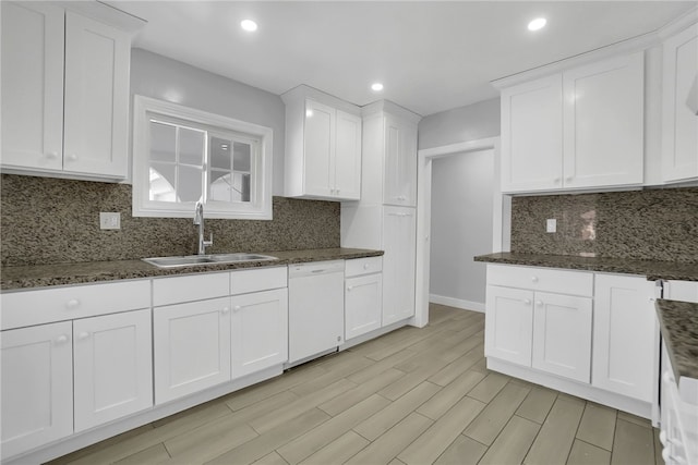 kitchen featuring white cabinets, dark stone counters, dishwasher, and sink