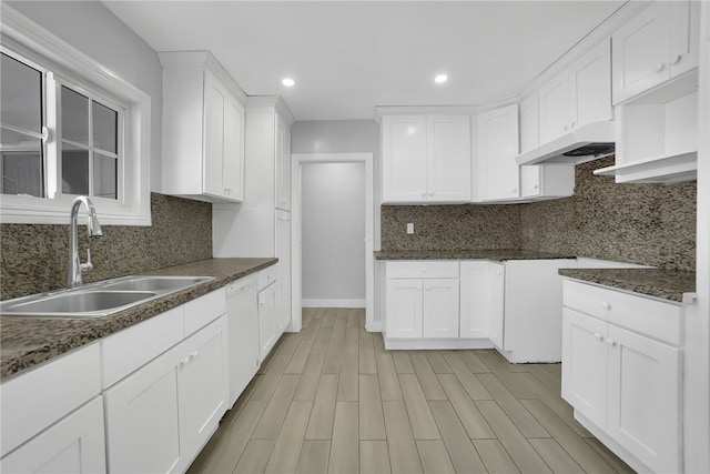 kitchen with sink, white dishwasher, white cabinets, and dark stone counters