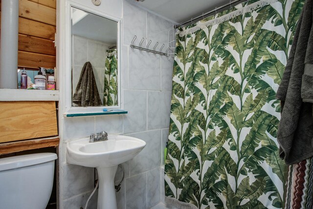 bathroom featuring tile walls, sink, curtained shower, and toilet