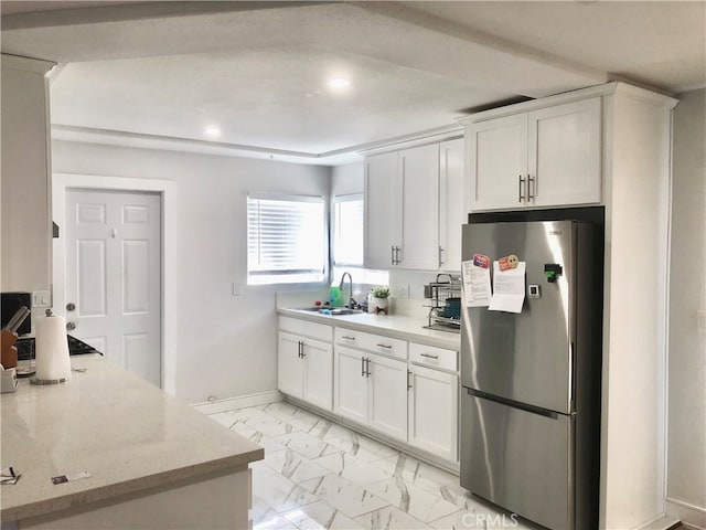 kitchen with white cabinets, light stone countertops, stainless steel fridge, and sink