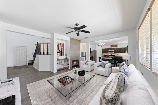 living room featuring ceiling fan with notable chandelier, hardwood / wood-style flooring, and a tile fireplace