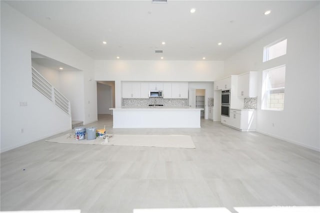 kitchen featuring decorative backsplash, open floor plan, appliances with stainless steel finishes, and white cabinets