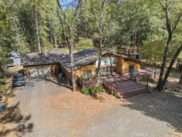 rustic home with a forest view, a wooden deck, driveway, and a garage