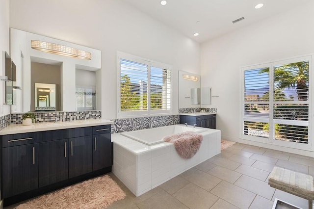 bathroom featuring tile patterned flooring, vanity, a wealth of natural light, and tiled bath