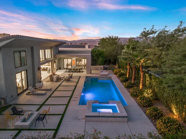 pool at dusk featuring an in ground hot tub and a patio area