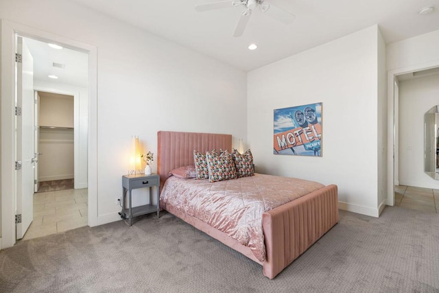 bedroom featuring a walk in closet, light colored carpet, a closet, and ceiling fan