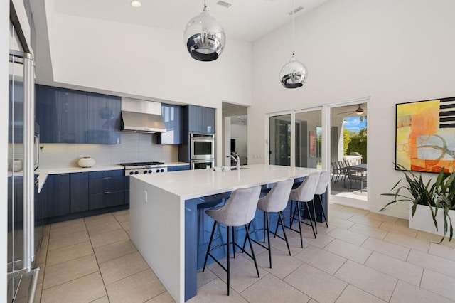 kitchen featuring a breakfast bar, backsplash, hanging light fixtures, a kitchen island with sink, and wall chimney exhaust hood