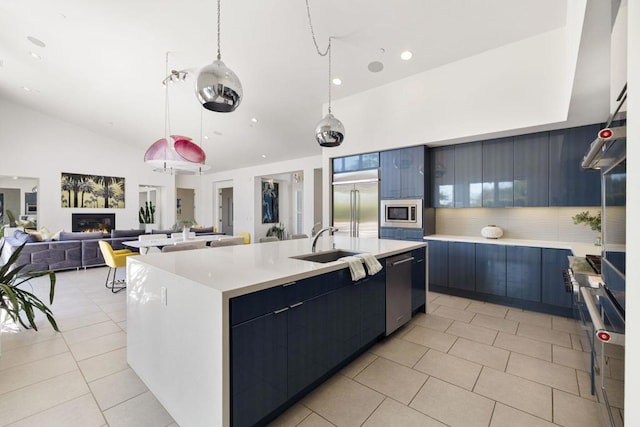 kitchen featuring sink, light tile patterned floors, built in appliances, decorative light fixtures, and a large island with sink