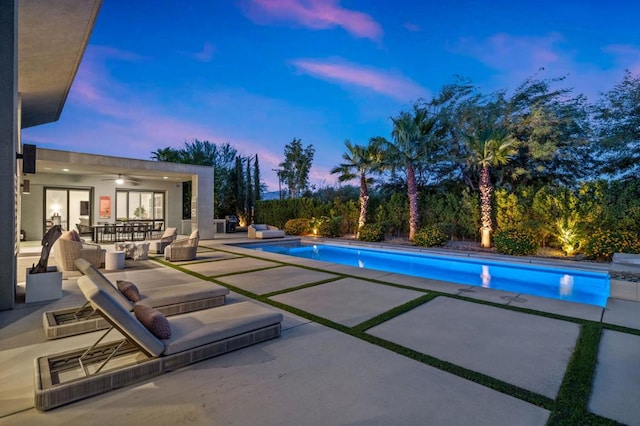 pool at dusk with ceiling fan, an outdoor living space, and a patio area