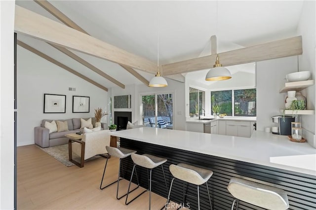 kitchen with sink, lofted ceiling with beams, kitchen peninsula, pendant lighting, and light hardwood / wood-style floors