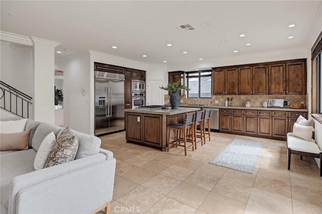 kitchen featuring backsplash, ornamental molding, a breakfast bar, built in appliances, and a kitchen island