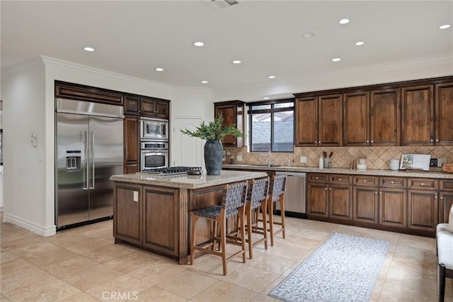 kitchen with light stone countertops, decorative backsplash, crown molding, built in appliances, and a center island