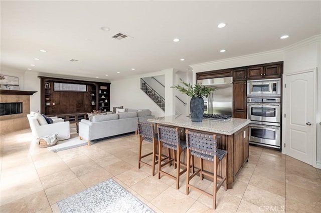 kitchen featuring built in appliances, light stone countertops, ornamental molding, a kitchen island, and a kitchen bar