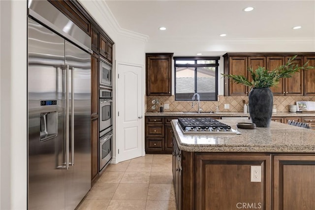 kitchen featuring a center island, stainless steel appliances, light stone counters, and crown molding