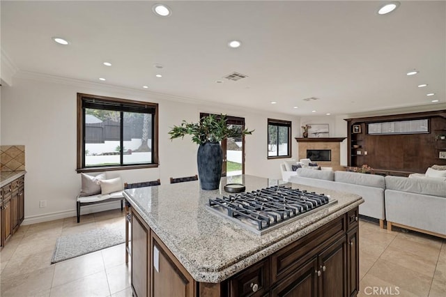 kitchen with a kitchen island, stainless steel gas cooktop, light stone counters, crown molding, and light tile patterned flooring