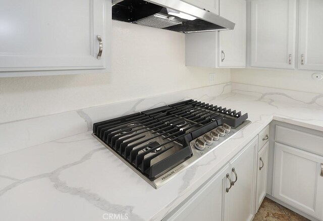 room details with stainless steel gas cooktop, white cabinetry, light stone counters, and ventilation hood