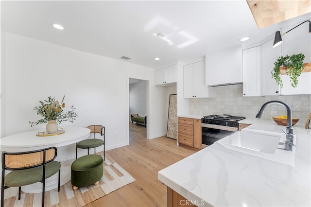 kitchen featuring light stone counters, light hardwood / wood-style floors, sink, white cabinetry, and black gas range