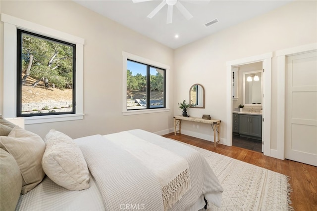 bedroom featuring ceiling fan, hardwood / wood-style flooring, multiple windows, and ensuite bathroom