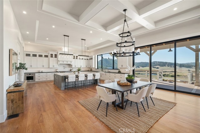 dining area featuring light hardwood / wood-style floors, coffered ceiling, a chandelier, and a mountain view