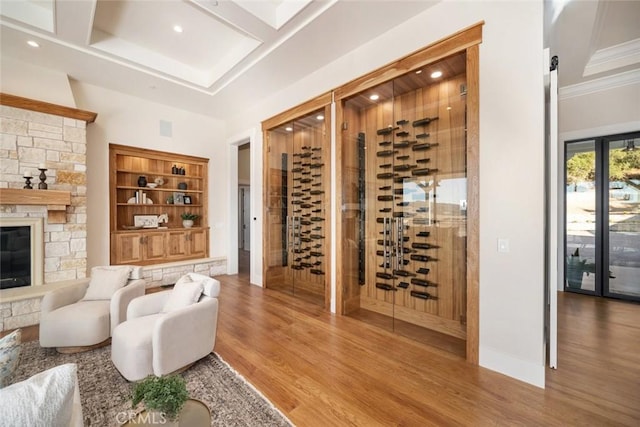 wine room featuring visible vents, coffered ceiling, wood finished floors, a stone fireplace, and baseboards