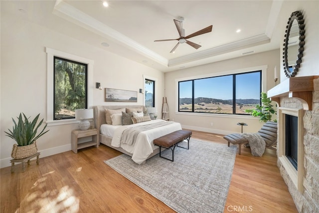 bedroom with light hardwood / wood-style floors, a raised ceiling, a fireplace, and ceiling fan