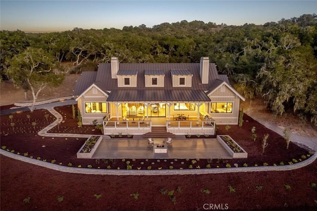 rear view of house featuring a forest view, metal roof, a chimney, and a standing seam roof