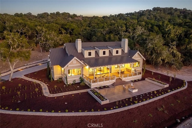 rear view of property featuring a standing seam roof, metal roof, a wooded view, and a chimney