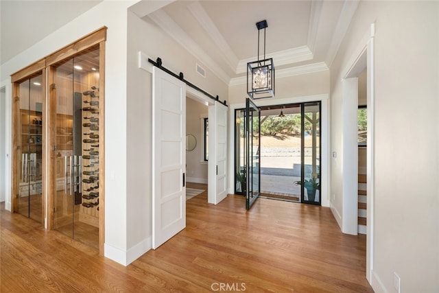 entryway featuring ornamental molding, light wood-type flooring, a raised ceiling, and a barn door