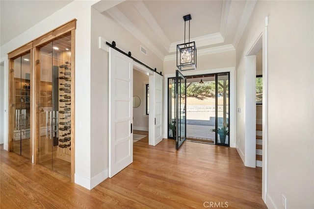 entrance foyer with visible vents, a tray ceiling, a barn door, crown molding, and light wood finished floors