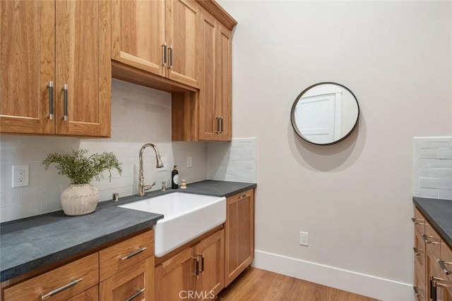 kitchen with a sink, decorative backsplash, baseboards, and dark countertops