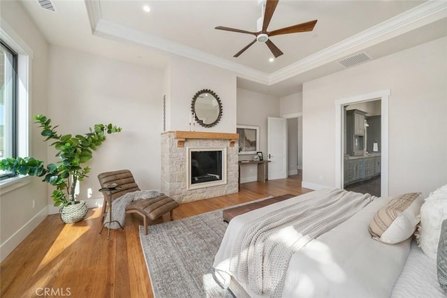 bedroom with wood finished floors, baseboards, visible vents, ornamental molding, and a stone fireplace