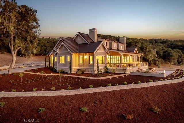 view of front of house with a standing seam roof, a porch, board and batten siding, metal roof, and a chimney