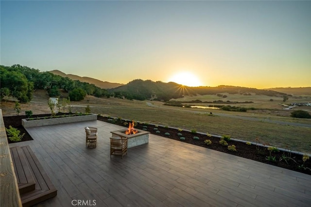 deck at dusk with a mountain view, a fire pit, and a rural view