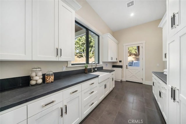 kitchen featuring visible vents, a sink, dark countertops, white cabinetry, and baseboards