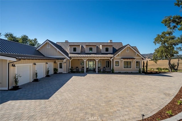 view of front of property with a standing seam roof, decorative driveway, an attached garage, metal roof, and a chimney