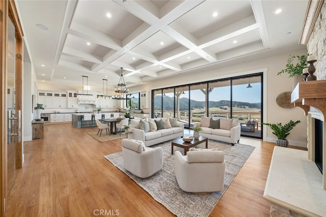 living room with light wood-type flooring, a mountain view, a chandelier, beam ceiling, and coffered ceiling