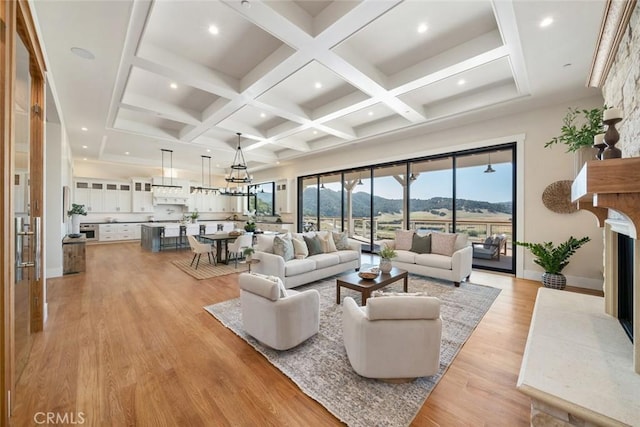 living area with coffered ceiling, beam ceiling, light wood-style flooring, a fireplace, and a mountain view