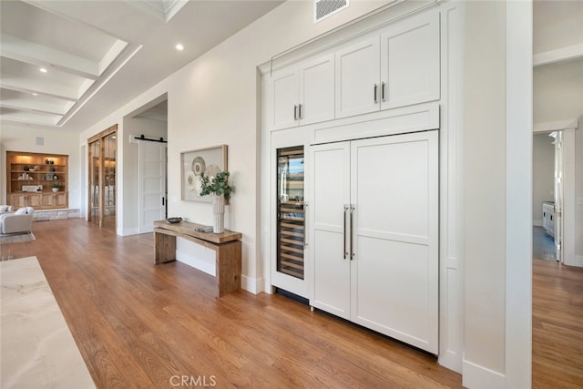 interior space with a barn door, light wood-type flooring, and beamed ceiling