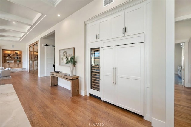 foyer entrance with a barn door, coffered ceiling, visible vents, and light wood finished floors