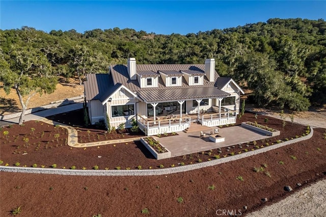 rear view of property with metal roof, a view of trees, a chimney, and a standing seam roof