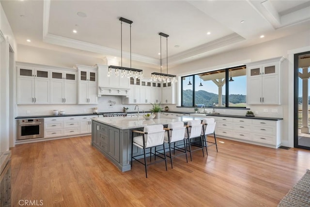 kitchen with oven, a tray ceiling, a breakfast bar, and light wood-style flooring