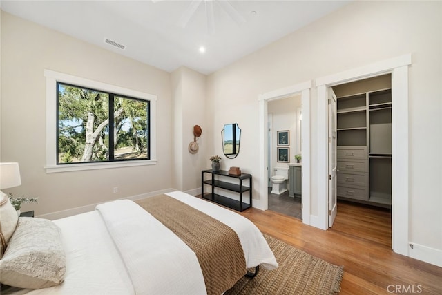 bedroom with ceiling fan, connected bathroom, a walk in closet, hardwood / wood-style flooring, and a closet