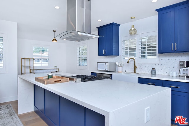 kitchen with decorative backsplash, island range hood, blue cabinetry, pendant lighting, and light hardwood / wood-style floors