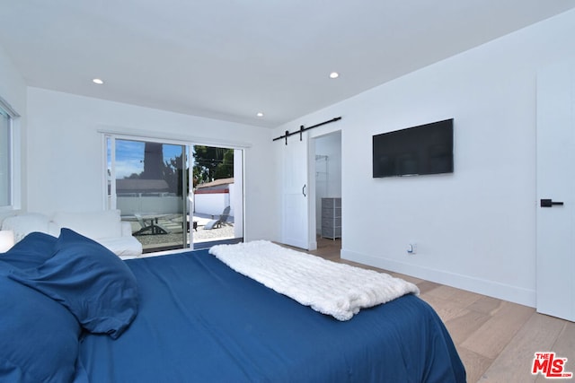 bedroom with a barn door, light hardwood / wood-style floors, and access to exterior