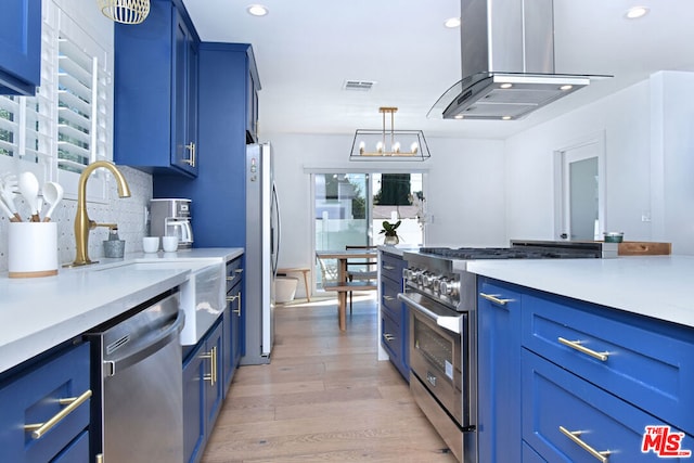 kitchen featuring island exhaust hood, appliances with stainless steel finishes, light wood-type flooring, blue cabinets, and pendant lighting